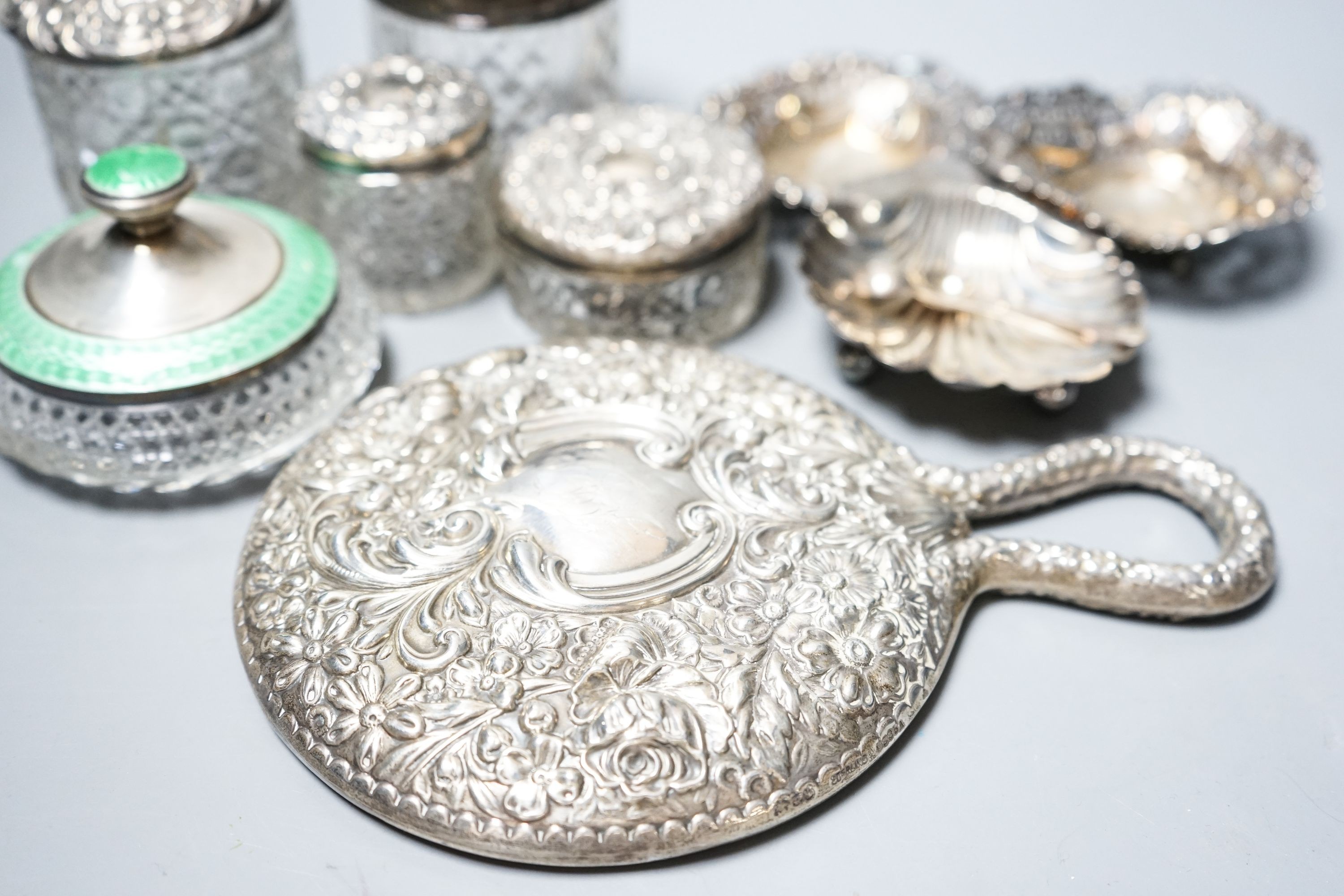 A silver and enamel mounted glass toilet jar, four other toilet jars, a hand mirror and three small silver dishes.